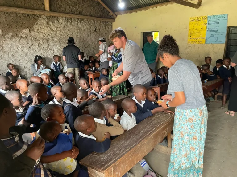 Missions team members handing out food to schoolchildren in a packed rural classroom
