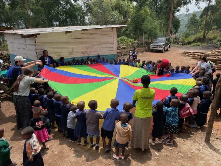 Children gathered around a colorful parachute outdoors participating in an activity led by the missions team